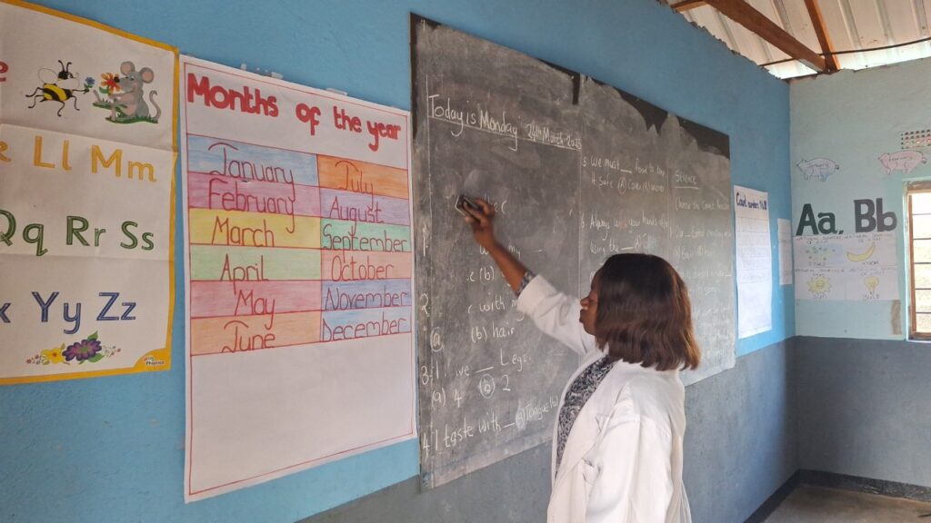 Madam Bertha cleaning the blackboard in a classroom at All Is Grace School, preparing for the day's first lesson