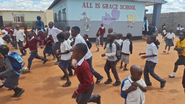 Children playing joyfully outside All Is Grace School, showing the impact of community education