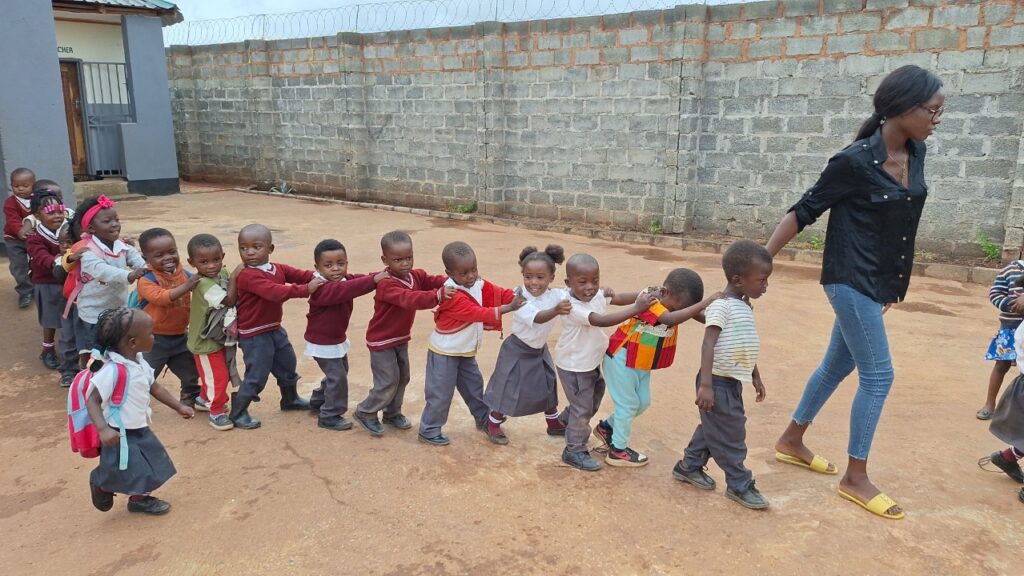 Young children following their teacher in a line at All Is Grace School