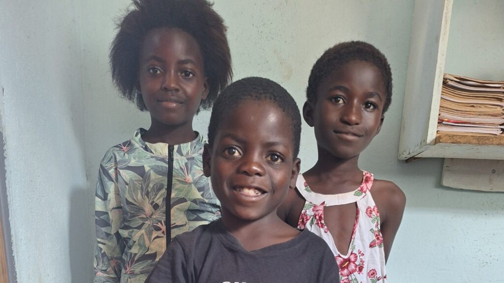 Three children at All Is Grace School wearing donated clothes for school