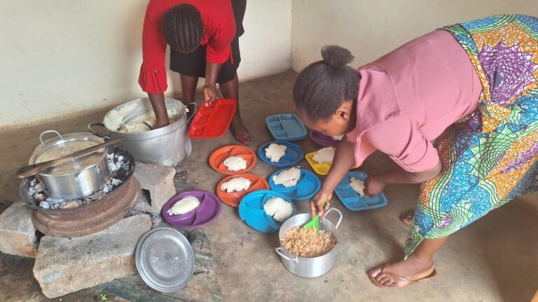 Two women prepare plates of nshima and beans as part of the school feeding program at All Is Grace School.