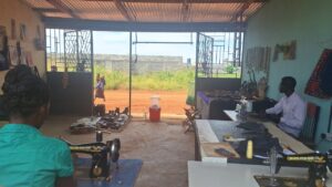 Tailoring Department at All Is Grace campus showing adults sewing, with crafts, shoes, and school uniforms as part of adult education opportunities