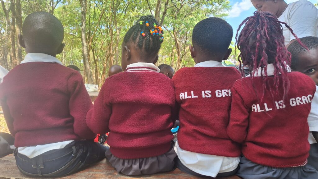 Children seated side by side on a bench during a school outing, wearing school uniforms.